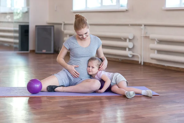Pregnant woman with her daughter doing gymnastics