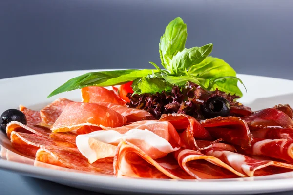 Sliced ham, prosciutto, bacon, salami and other meat delicacies are on the plate.