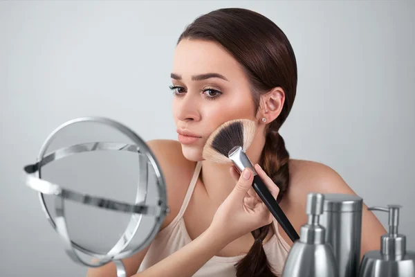 Girl, woman in the mirror puts makeup brush