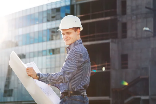 Architect in helmet with blueprints looks at camera in building site
