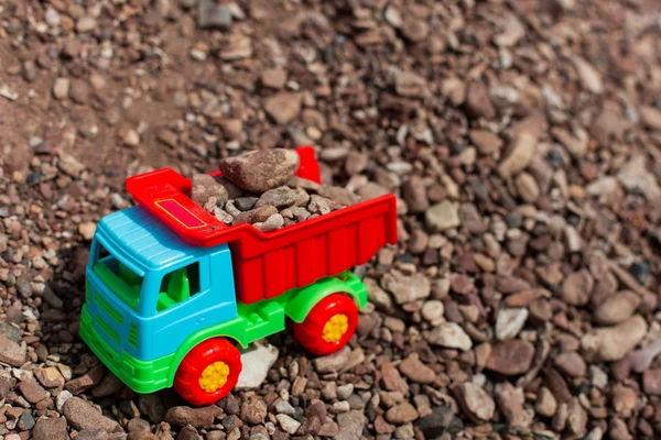 Multi-colored toy truck against a backdrop of sand and stones