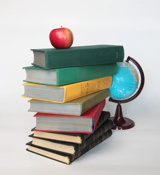Pile of old books with apple on top and globe