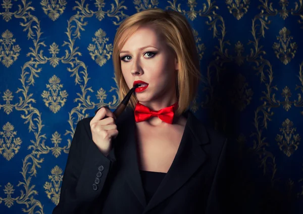 Young blonde with red lips and smoking pipe dressed in a men\'s suite