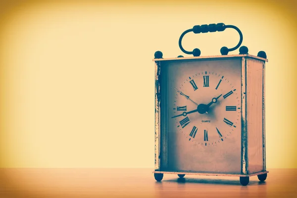 Retro styled image of vintage square table clock on a wooden table.