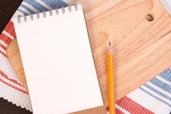 Notebook for culinary recipes on a cutting board with napkin. Open recipe book on wooden background.