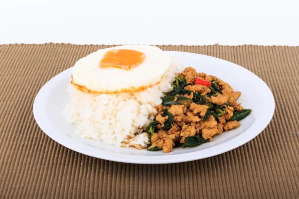 Rice topped with stir-fried chicken, basil and fried egg on white background