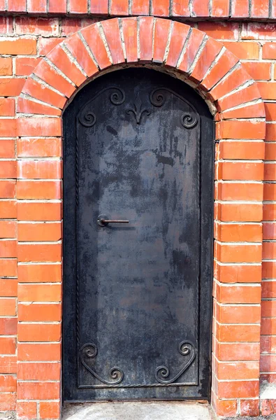 Stone and metal. Red orange brick wall with a frame for a door. The arch of brick and black steel with a pattern from the street.