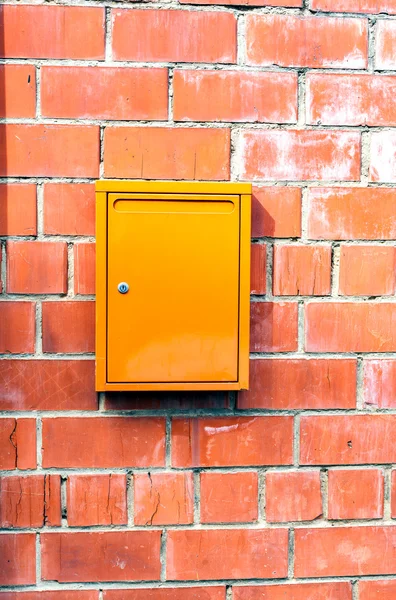 Stone and metal. Red orange brick wall orange mailbox. The texture of the surface of a brick wall with a box for letters from the street.