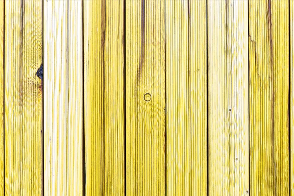 A fragment of an old wooden fence. Painted wooden planks as a background with copy space. Wooden rustic background or painted wood boards texture. Old peeling yellow paint.
