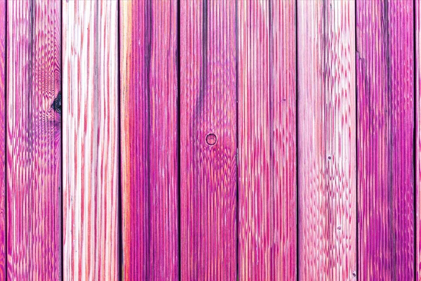 A fragment of an old wooden fence. Painted wooden planks as a background with copy space. Wooden rustic background or painted wood boards texture. Old peeling pink paint.