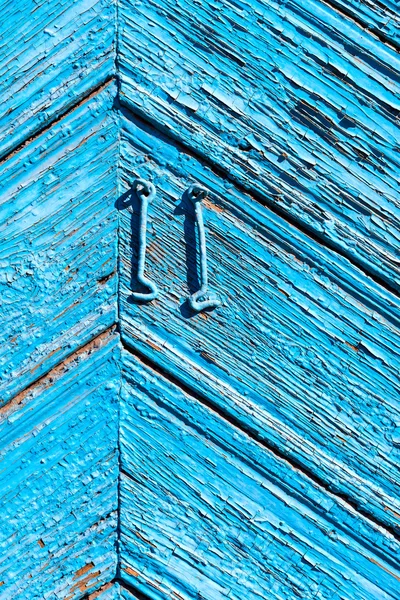 A fragment of a wooden door blue. Painted wooden planks as a background with copy space. Texture old peeling paint, the board of diagonally. Rural background bright blue and two old metal hook.