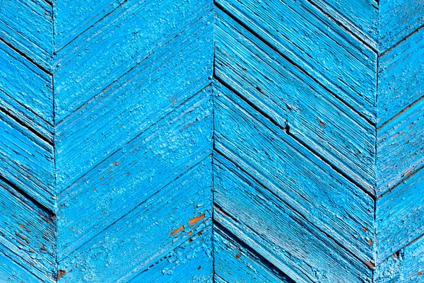 A fragment of a wooden door blue. Painted wooden planks as a background with copy space. Texture old peeling paint, the board of diagonally. Rural background bright blue