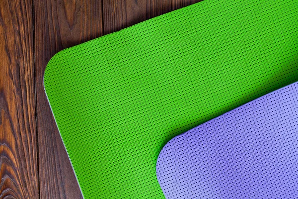 New yogamat green and purple on a wooden background. Facilities for training and yoga. Diagonal. The concept of love to a healthy lifestyle. Weight loss and fitness.