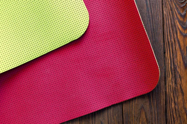 New yoga mat of red and yellow on a wooden background. Facilities for training and yoga. Diagonal. The concept of love to a healthy lifestyle. Weight loss and fitness.