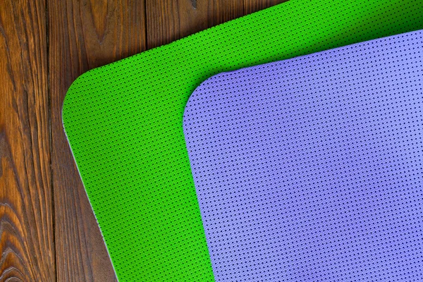 New yogamat green and purple on a wooden background. Facilities for training and yoga. Diagonal. The concept of love to a healthy lifestyle. Weight loss and fitness.
