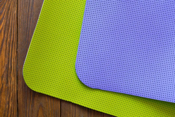 New yogamat green and purple on a wooden background. Facilities for training and yoga. Diagonal. The concept of love to a healthy lifestyle. Weight loss and fitness.