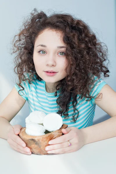 Portrait of a young girl with brown curly hair. It keeps holding vase with white marshmallows. Eastern sweetness. Gentle and dreamy look. Good morning. Dessert for breakfast