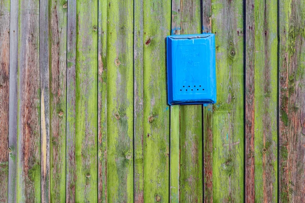 Wooden boards as a background and a mailbox. The texture of the fence. Vintage effect. Boards old peeling green paint and blue mailbox for letters. Copy space.