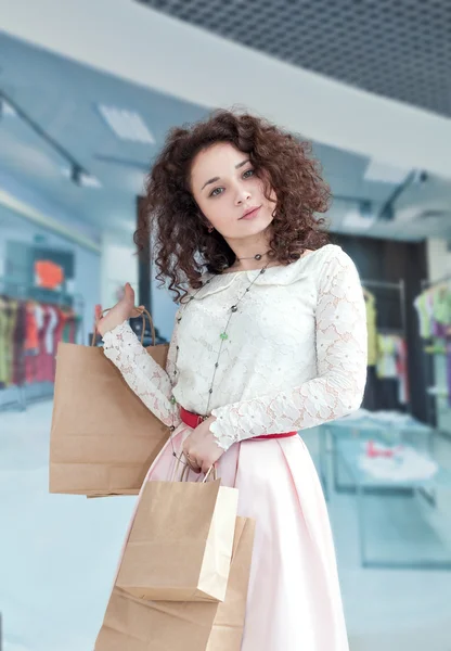 Caucasian girl in the mall shopping. Portrait of a girl with shopping bags on the background of shop window. Happy shopper.