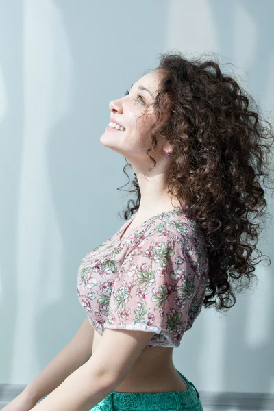Young girl with curly hair smiling and enjoying life. Portrait in profile looking up. Tender feelings. Meditation. Practice yoga at home. Exercising in the morning in the bright sun room.