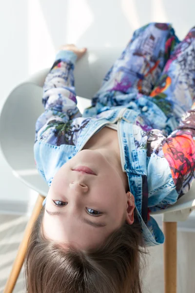 Portrait of a little girl of fashion baby on a white chair. Stylish little girl with long hair sits upside down. Photo model child cool fashionable.