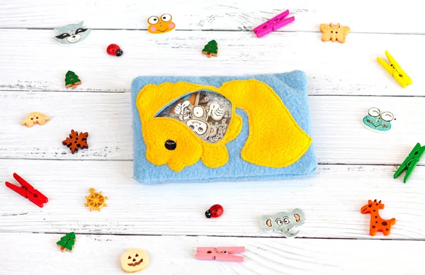 Childrens toys made of colored fleece for motor development. Bag with yellow fish fleece filled with plastic beads and figurines on a white wooden background. handmade toys. Happy childhood.