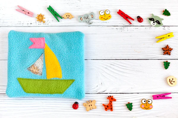 Childrens toy made of colored fleece for motor development. Pouch with a ship of the fleece filled with plastic beads and figurines on a white wooden background. handmade toys. Happy childhood.