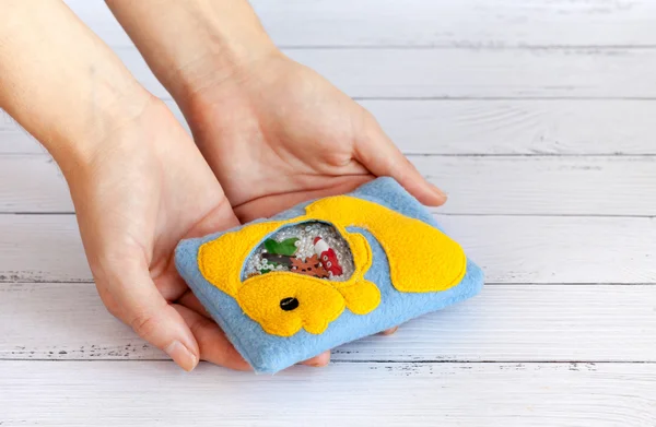 Childrens toy made of colored fleece for the development motor skills in the hands women. Bag with yellow fish filled plastic beads and figurines on a white wooden background. handmade toys