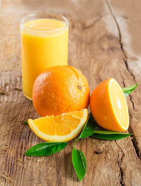 Glass of orange juice  with cut orange and leaves on wooden back