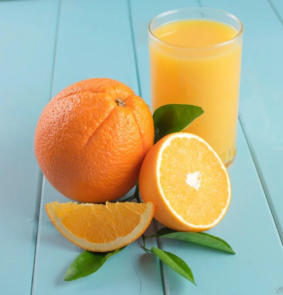 Glass of orange juice  with cut orange and leaf on blue wooden b