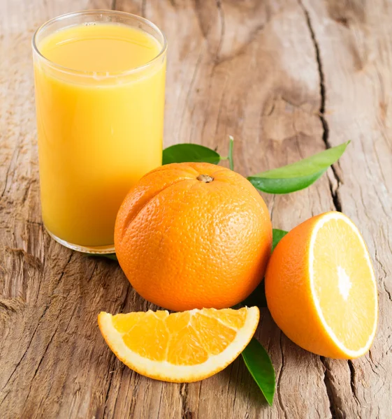 Glass of orange juice  with cut orange and leaves on wooden back