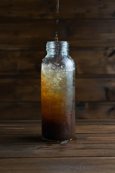 Filling water into a bottle of iced coffee on a wooden backgroun