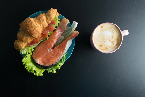 Croissant with salmon, lettuce on blue plate and pink cup of cof