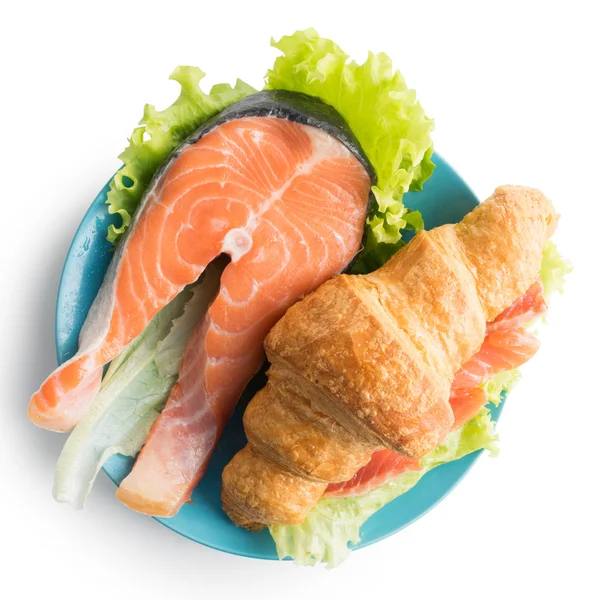 Croissant with salmon, lettuce on blue plate and cup of coffee o