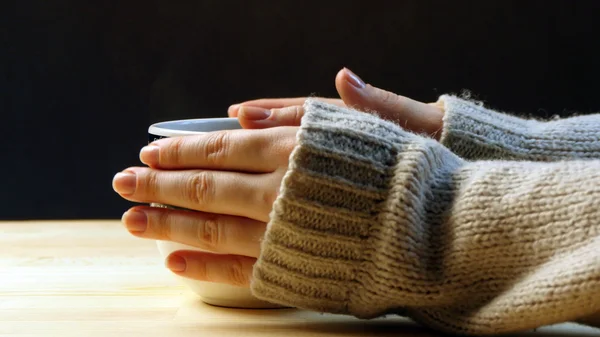 Woman holding cup of coffee, warming her hands.
