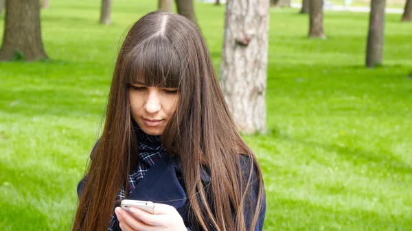 Beautiful woman uses cell smartphone outdoors in the park  - detail . Young attractive happy girl relaxes in a city park and uses a mobile phone. She looks very happy and contented