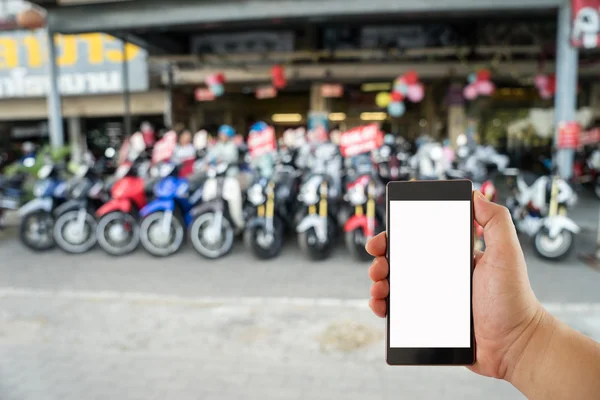 Hand holding mobile phone on motorcycle shop background