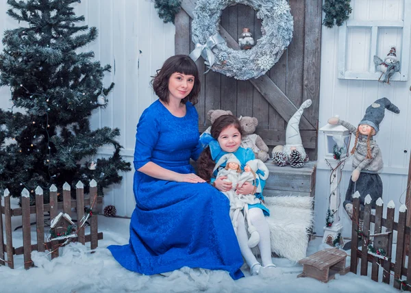 Happy mother with her daughter in long blue dresses  stand near the Christmas tree