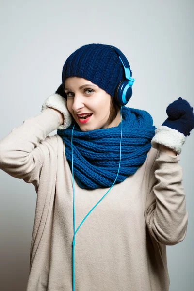 Cute girl listening to music with headphones in the winter, dressed in winter clothes, bright lifestyle photo, isolated on a gray background