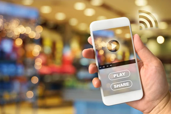 Woman hand holding smartphone against blur bokeh of shop backgro