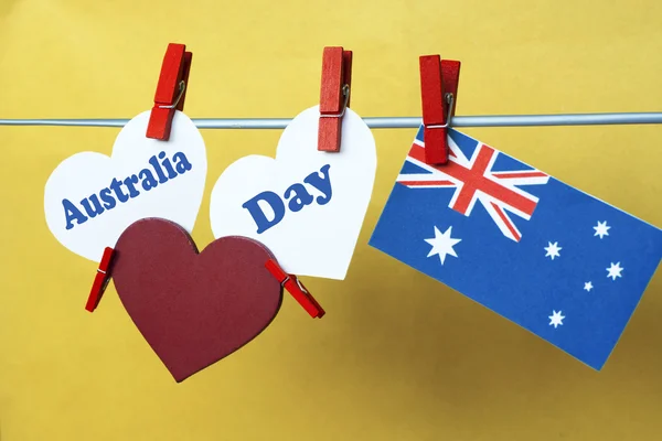 Celebrate Australia Day holiday on January 26 with a Happy Australia Day message greeting written across white Australian maps (red heart) and flag hanging pegs on yellow background. Toned collage