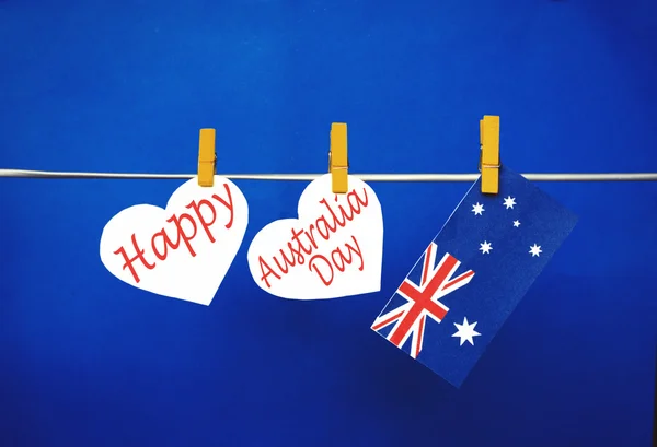 Celebrate Australia Day holiday on January 26 with a Happy message greeting written across white hearts, Australian flag hanging on pegs ( clothespin ) against red background. Toned collage