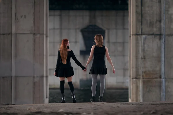 Two girls holding their hands together under urban bridge.