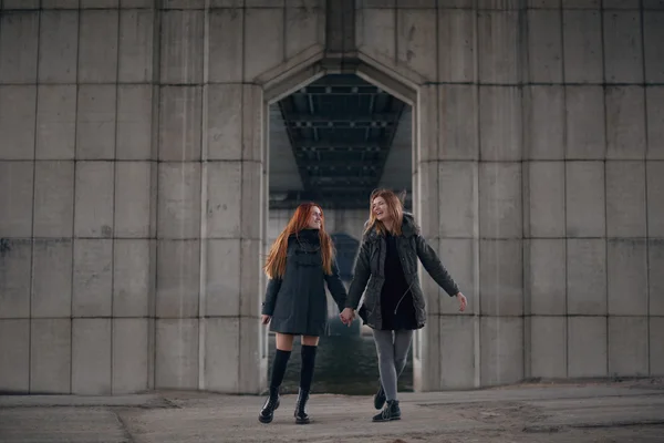 Two girls holding their hands together under urban bridge.