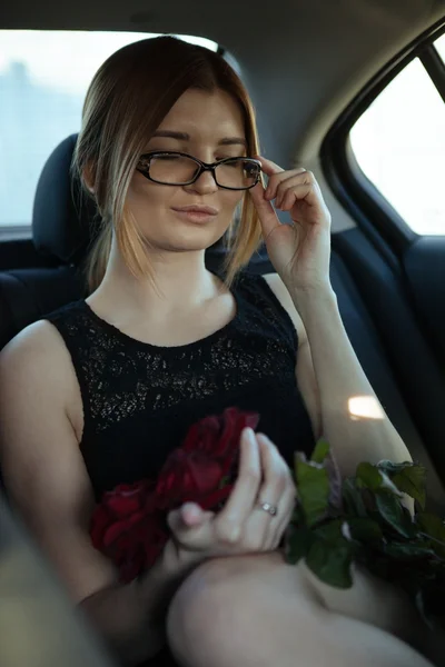 Girl in glasses at the backseat holding roses.