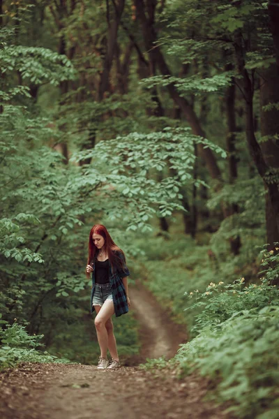 Young redhead girl walking through fresh green forest. Tourism concept.