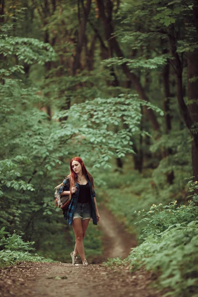 Young redhead girl walking through fresh green forest. Tourism concept.