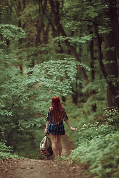 Young redhead girl walking through fresh green forest. Tourism concept.