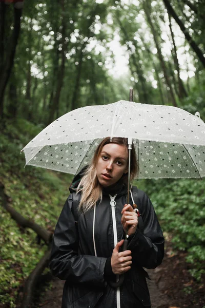 Young girl walking through a rainy forest with umbrella.