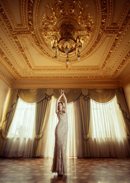 Beautiful girl in long dress flying in golden baroque interior.